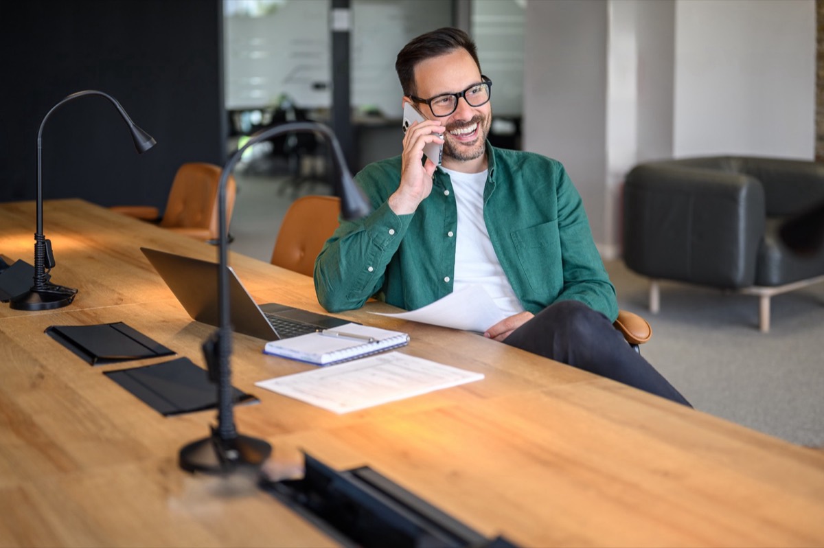Hombre sonriendo mientras habla por teléfono en su escritorio
