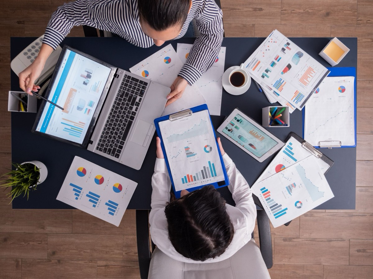 Dos personas revisando gráficas de ventas en una laptop y en hojas impresas